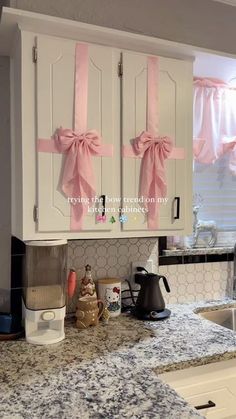 a kitchen with white cabinets and pink bows on the door handles that are tied to them