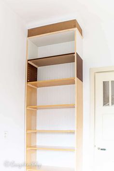 an empty bookcase in the corner of a room with white walls and wood shelves