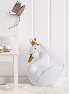 a white swan with a gold crown on its head sitting in front of a chair