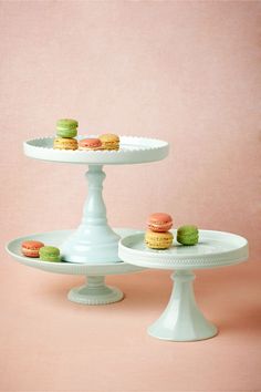 two tiered trays with small cakes on them sitting next to each other in front of a pink wall