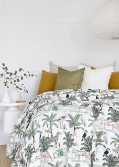 a bed with white and green comforter next to a plant in a vase on the floor