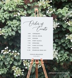 an easel with a sign that says order of events on it and flowers in the background