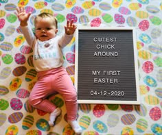 a baby laying on top of a blanket next to a sign that says cutest chick around my first easter