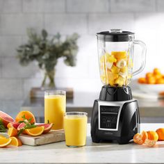 a blender filled with fruit sitting on top of a counter next to sliced oranges