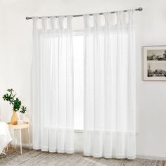 a bedroom with white walls and curtains on the windowsill