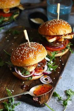 two burgers with toothpicks in them sitting on a cutting board next to other food