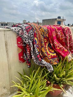 there are many scarves hanging on the clothes line above some potted planters