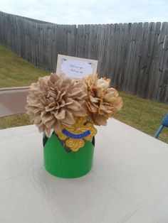 there is a green vase with flowers in it sitting on the table near a fence