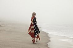 a woman is walking on the beach holding an american flag