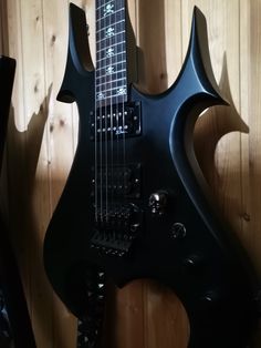 a black electric guitar sitting on top of a wooden wall