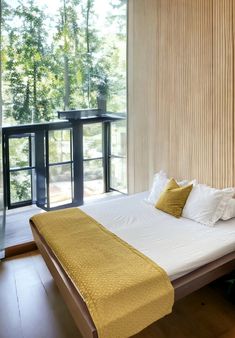 a bed with white sheets and yellow pillows in a bedroom next to sliding glass doors