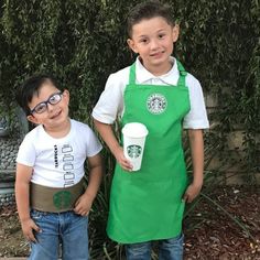 two young boys wearing green aprons and holding starbucks cups in front of a bush