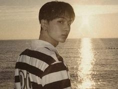 a young man standing on top of a beach next to the ocean in front of the sun