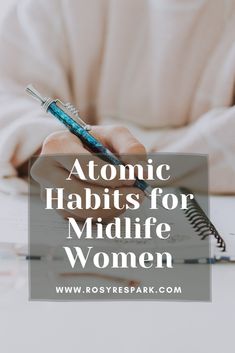 a woman writing on top of a book with the words atomic habitts for midlife women