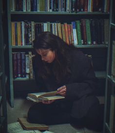 a woman sitting on the floor reading a book in front of a bookshelf