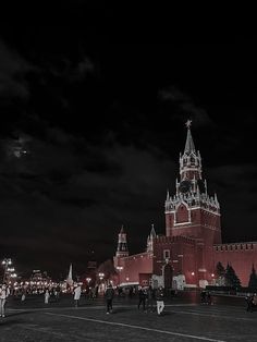 people are walking around in front of the red brick building with white spires at night