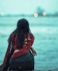 a woman sitting on the edge of a pier looking out at the ocean with lights in the background