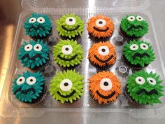 cupcakes decorated with green, orange and black icing are in a plastic container