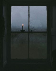 a candle sitting on top of a window sill in front of a rain covered window