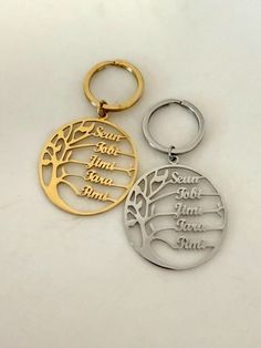 two metal keychains with engraved names and tree design on them, one is gold and the other is silver