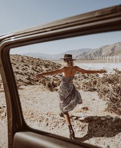 a woman in a dress and hat is reflected in a car's rear view mirror