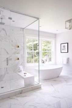 a large white bathroom with marble flooring and glass shower doors, windows, and a freestanding tub