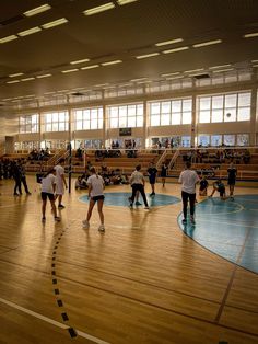 several people are playing volleyball in an indoor gym with wood floors and large windows on the wall