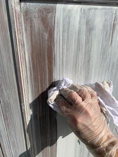 a person's hand holding something in front of a wooden door with peeling paint on it