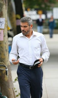 a man in white shirt and blue pants walking down the street with his cell phone