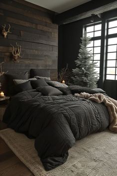 a bed with black comforter and pillows in front of a wooden wall next to a window