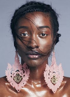 a woman with her hair blowing in the wind and wearing large pink earrings on her face