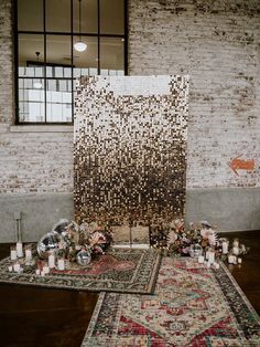 an area with rugs, candles and flowers on the floor in front of a brick wall