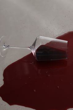 a wine glass sitting on top of a table covered in red liquid and spilled over it