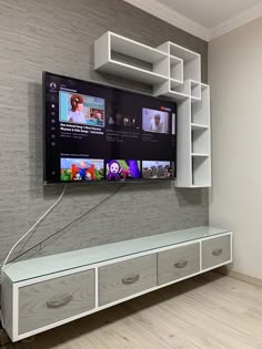 a flat screen tv mounted to the side of a wall next to drawers and a shelf