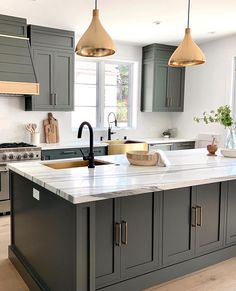 a kitchen with gray cabinets and white counter tops, two pendant lights over the island