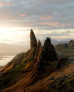 some very tall rocks on a hill by the water and clouds in the sky at sunset