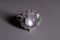 Fine jade ring set with high quality 'glassy' white (main) and green (small) jadeite cabochons and accented with diamonds in 18k. The jade has a very fine grain crystal and is noted for its transparency. In jadeite, this '玻璃种' or glassy type is distinguished from mere icy or translucent jade. Glassy jadeite has the topmost clarity in terms of transparency. Specifically, these is icy white jade that displays an optical phenomenon known in the jade trade as '起莹光' or luminescence. Luminescence appears as a silvery white light moving through the jade cabochon. The phenomenon is not the reflection of light/lamp but pushed from within the stone. If present, this phenomenon is mostly observed in top quality icy white jadeite, and less commonly in icy green jadeite. "Every jade is unique": this di Elegant White Jade Ring, Elegant Green Cabochon Moonstone Ring, Optical Phenomena, Jade Ring, White Jade, Light Reflection, Light Lamp, Rings Statement, Ring Set