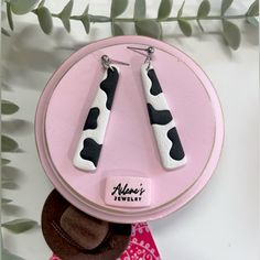 two pairs of earrings with black and white cow print on them sitting on a pink plate