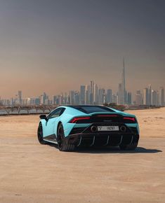 the rear end of a blue sports car in front of a large cityscape