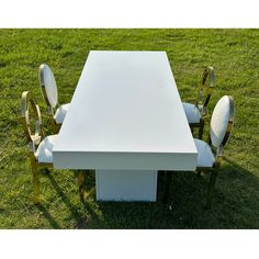 a white table with four chairs around it on the grass in front of a grassy field