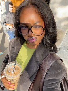 a woman wearing glasses and holding a drink in her hand while standing on the street