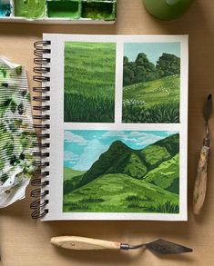 an open notebook with pictures of green hills and trees on the pages next to some paintbrushes