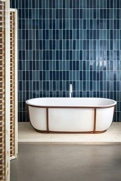 a bathtub in front of a blue tiled wall with wood trim around the edge