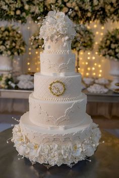 a wedding cake with white flowers on the side and gold monogrammed topper