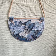 a woman's white sweater with blue butterflies on it and a brown leather purse hanging from the shoulder