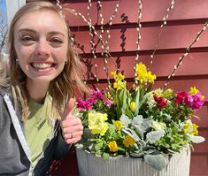 a woman sitting next to a potted plant with yellow and pink flowers in it