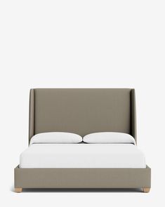 an upholstered bed with two pillows and white linens on the headboard