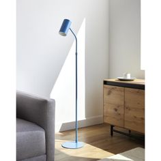 a blue floor lamp sitting on top of a hard wood floor next to a gray couch