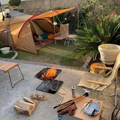 an outdoor fire pit surrounded by chairs and tables with a tent in the back ground