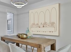 a dining room table with white chairs and a large drawing on the wall above it